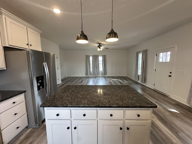 kitchen with open floor plan, dark stone countertops, wood finished floors, stainless steel refrigerator with ice dispenser, and pendant lighting