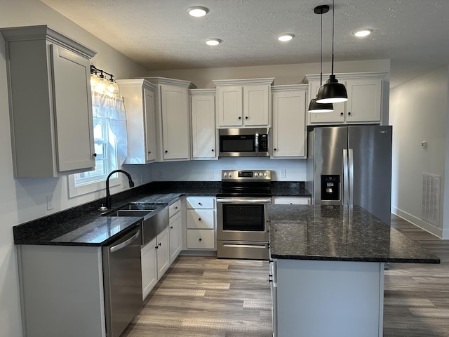 kitchen with visible vents, a kitchen island, stainless steel appliances, light wood-type flooring, and a sink