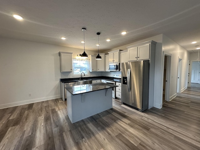 kitchen with dark wood-type flooring, a kitchen island, baseboards, appliances with stainless steel finishes, and dark countertops