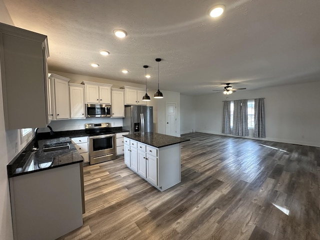 kitchen with white cabinets, dark wood finished floors, a kitchen island, stainless steel appliances, and a sink