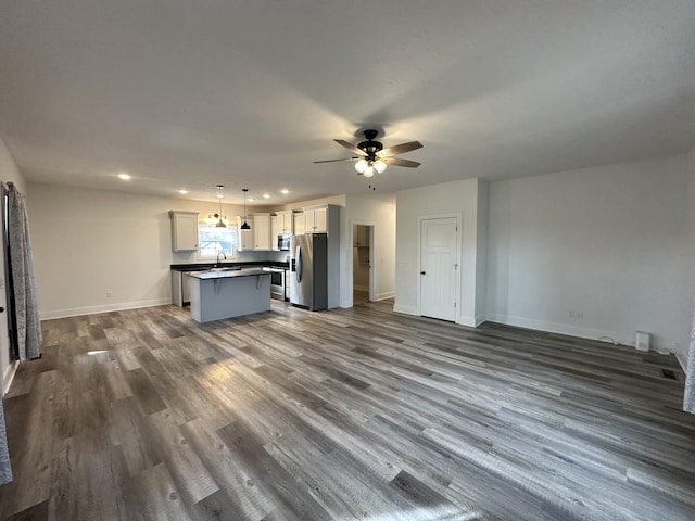 kitchen with dark wood-style flooring, open floor plan, dark countertops, stainless steel fridge, and a center island with sink