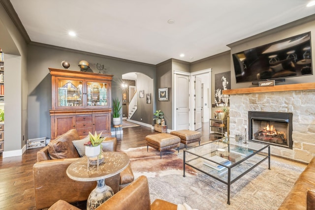 living area featuring arched walkways, a fireplace, wood finished floors, baseboards, and stairs