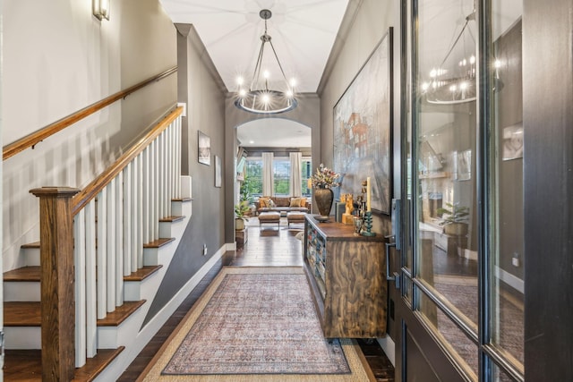 entrance foyer featuring arched walkways, a notable chandelier, dark wood finished floors, baseboards, and stairs