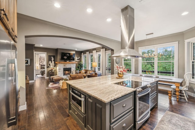 kitchen featuring light stone counters, a center island, island exhaust hood, appliances with stainless steel finishes, and a stone fireplace