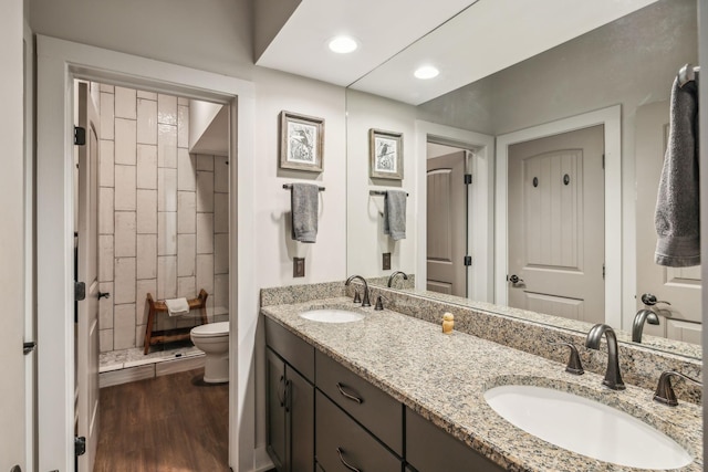 full bathroom with double vanity, a sink, toilet, and wood finished floors