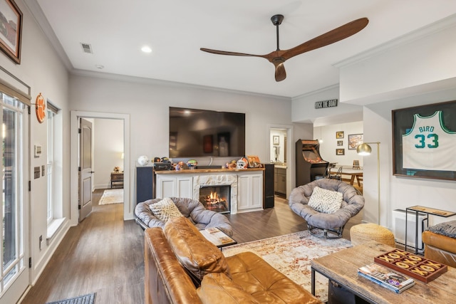 living area featuring ceiling fan, dark wood-style flooring, crown molding, and a high end fireplace