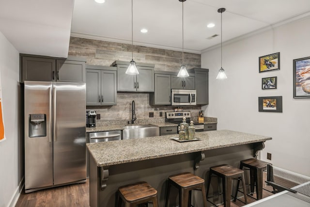 kitchen featuring light stone counters, a breakfast bar, hanging light fixtures, stainless steel appliances, and a sink