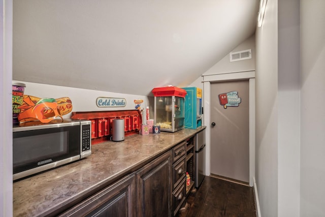 kitchen featuring stainless steel microwave, visible vents, dark wood-type flooring, vaulted ceiling, and dark brown cabinetry