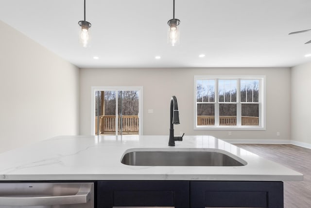 kitchen with dishwashing machine, light stone counters, a sink, a healthy amount of sunlight, and open floor plan