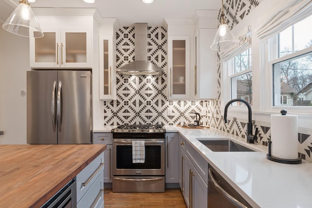 kitchen with wall chimney exhaust hood, sink, appliances with stainless steel finishes, gray cabinets, and pendant lighting