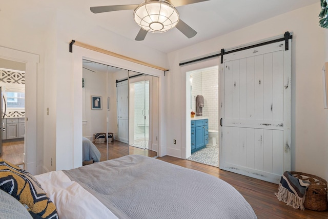 bedroom with dark wood-type flooring, ensuite bath, stainless steel fridge, and a barn door