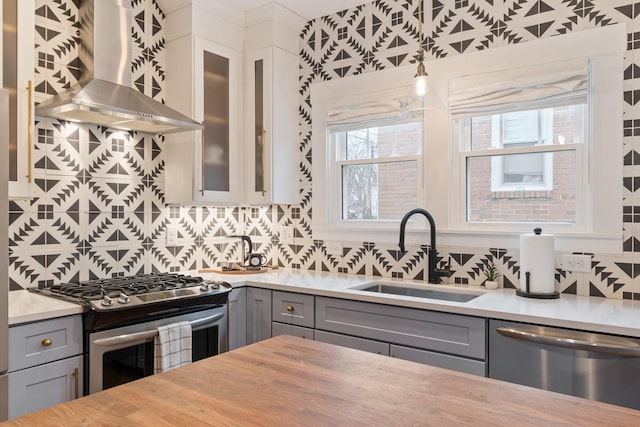 kitchen featuring appliances with stainless steel finishes, white cabinetry, sink, gray cabinetry, and wall chimney range hood