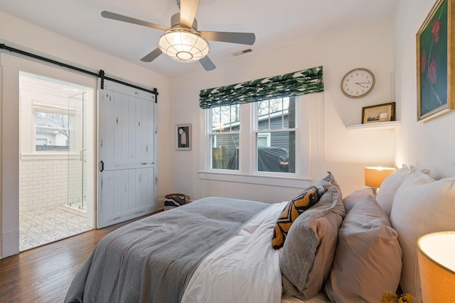 bedroom featuring ensuite bathroom, a barn door, dark wood-type flooring, and ceiling fan