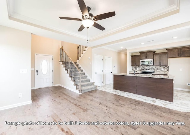 kitchen featuring stainless steel appliances, ornamental molding, light wood-type flooring, and a tray ceiling