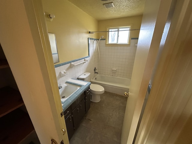 full bathroom with toilet, a textured ceiling, tile walls, vanity, and tiled shower / bath combo