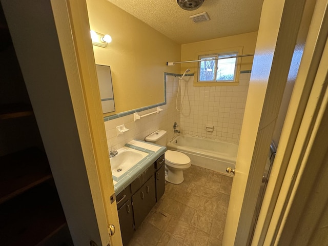 full bathroom featuring tiled shower / bath, tile walls, vanity, toilet, and a textured ceiling