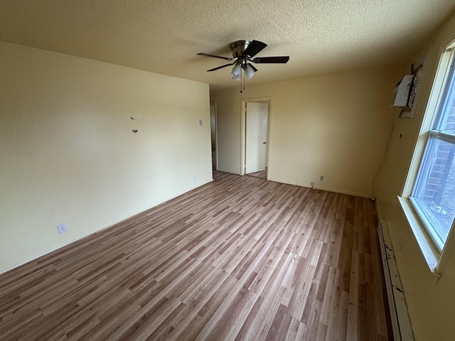 empty room with light wood-type flooring, a wall mounted AC, ceiling fan, baseboard heating, and a textured ceiling