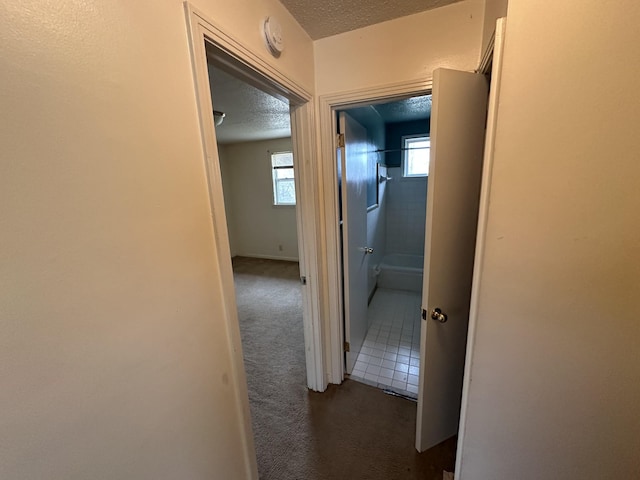 corridor with a textured ceiling and dark colored carpet