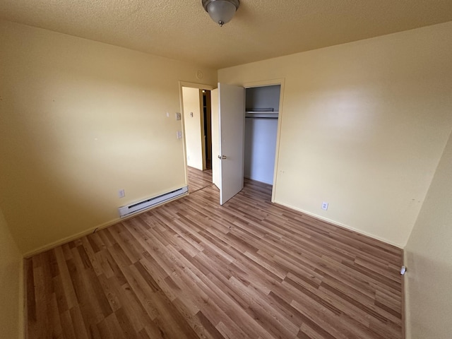 unfurnished bedroom with hardwood / wood-style flooring, a closet, a textured ceiling, and baseboard heating