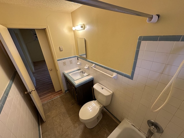 full bathroom featuring bathtub / shower combination, tile walls, vanity, toilet, and a textured ceiling