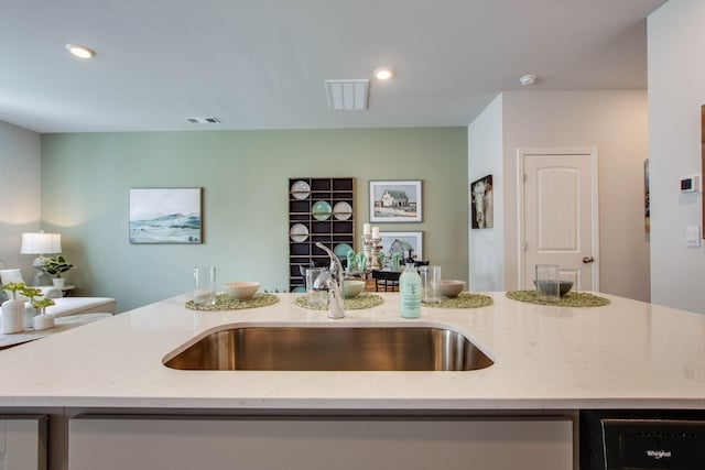 kitchen with light stone countertops, sink, and a center island with sink