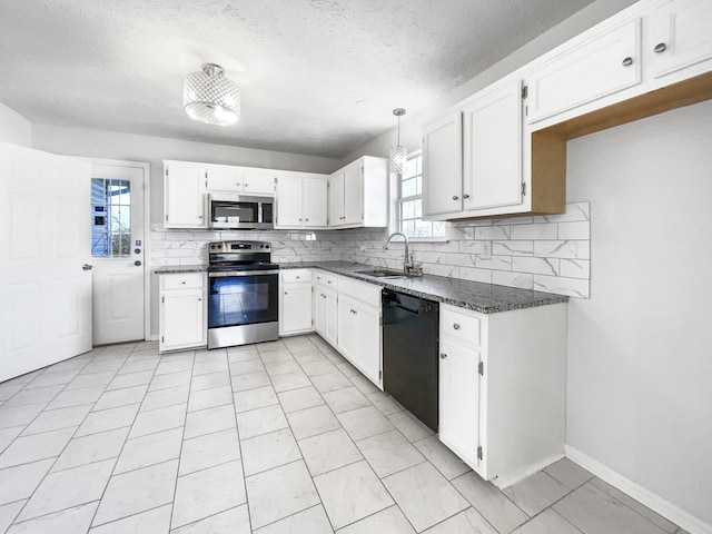 kitchen with appliances with stainless steel finishes, pendant lighting, white cabinetry, sink, and dark stone counters