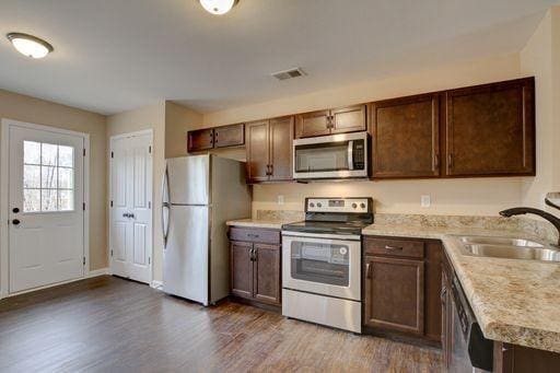 kitchen with stainless steel appliances, sink, dark brown cabinetry, and dark hardwood / wood-style flooring