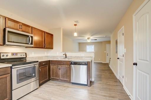 kitchen with sink, hanging light fixtures, stainless steel appliances, light hardwood / wood-style floors, and kitchen peninsula