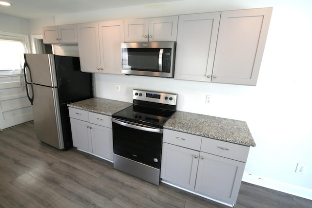 kitchen with stainless steel appliances, light stone counters, and dark wood-type flooring