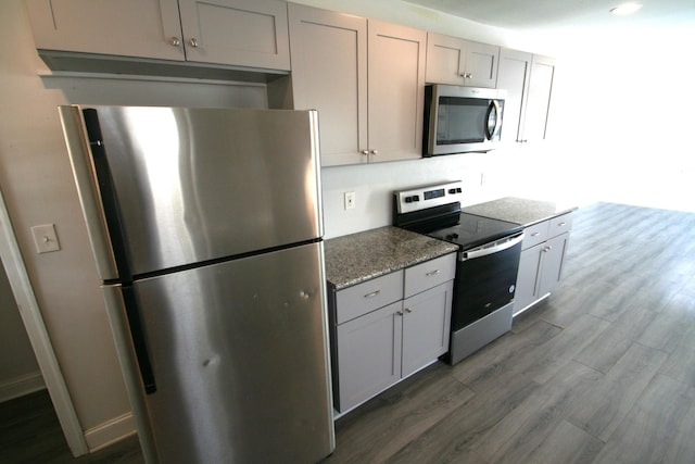 kitchen featuring stainless steel appliances, baseboards, dark wood finished floors, and light stone counters