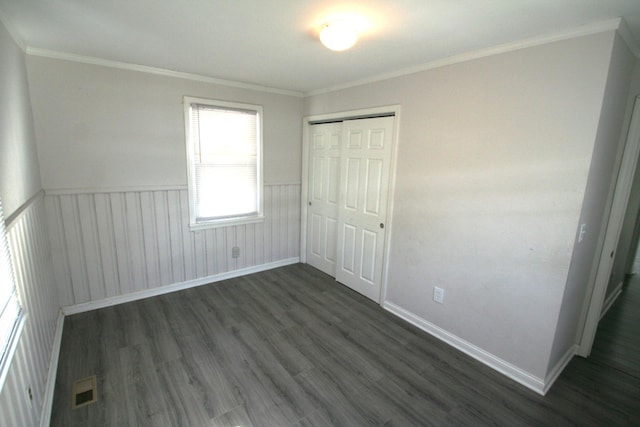 unfurnished bedroom with a wainscoted wall, dark wood-style flooring, visible vents, ornamental molding, and a closet