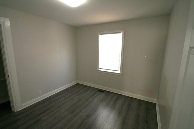 unfurnished room featuring dark wood-style flooring, visible vents, and baseboards