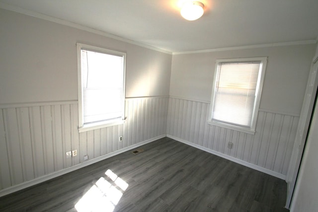 spare room featuring ornamental molding, dark wood-style flooring, wainscoting, and visible vents