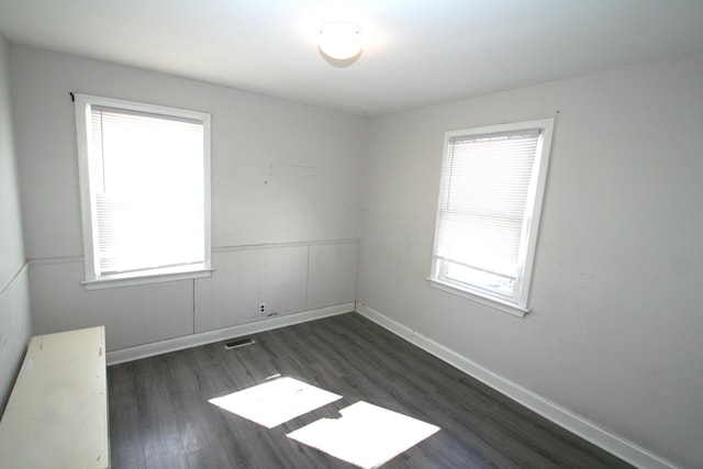 spare room with dark wood-type flooring, a wainscoted wall, visible vents, and baseboards