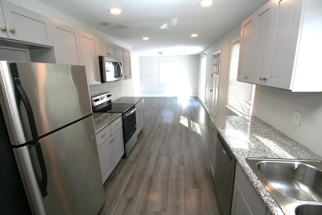 kitchen featuring light stone counters, recessed lighting, dark wood-type flooring, a sink, and appliances with stainless steel finishes