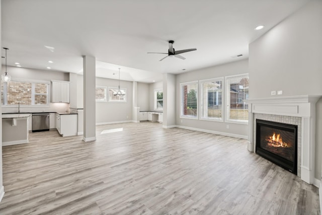 unfurnished living room with ceiling fan with notable chandelier, a fireplace, and light wood-type flooring