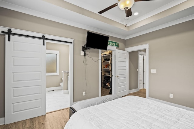 bedroom featuring hardwood / wood-style flooring, ornamental molding, a spacious closet, a raised ceiling, and a barn door