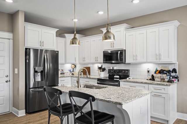 kitchen featuring white cabinetry, stainless steel appliances, decorative light fixtures, and an island with sink