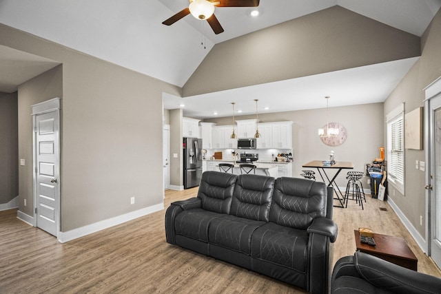 living room with ceiling fan with notable chandelier, high vaulted ceiling, and light hardwood / wood-style floors