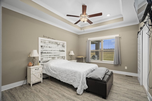 bedroom featuring crown molding, ceiling fan, wood-type flooring, and a tray ceiling