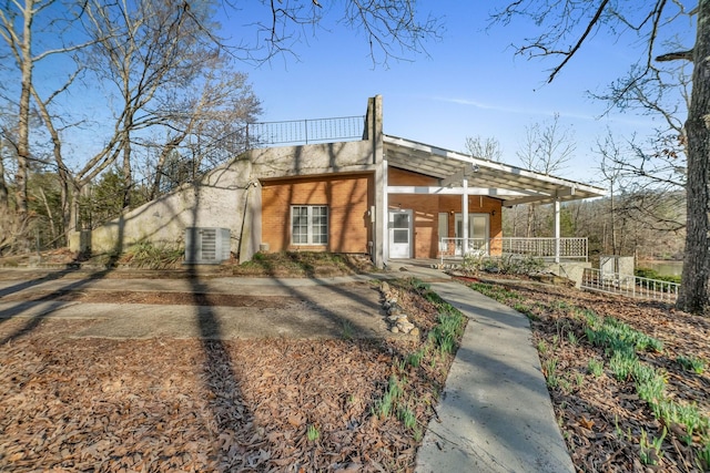 view of front facade with a porch, cooling unit, and brick siding