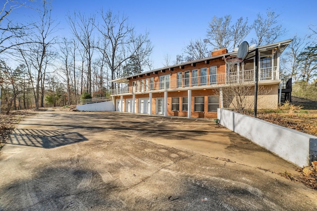 rear view of property with concrete driveway, brick siding, a chimney, and an attached garage