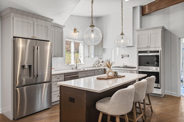 kitchen with appliances with stainless steel finishes, hanging light fixtures, a kitchen island, and gray cabinetry