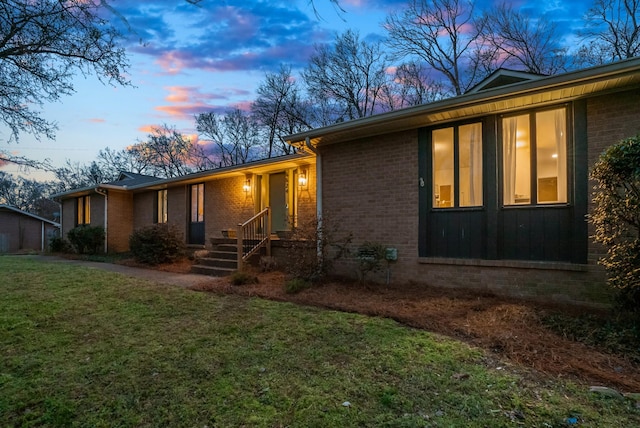 view of front of home featuring brick siding, a lawn, and board and batten siding