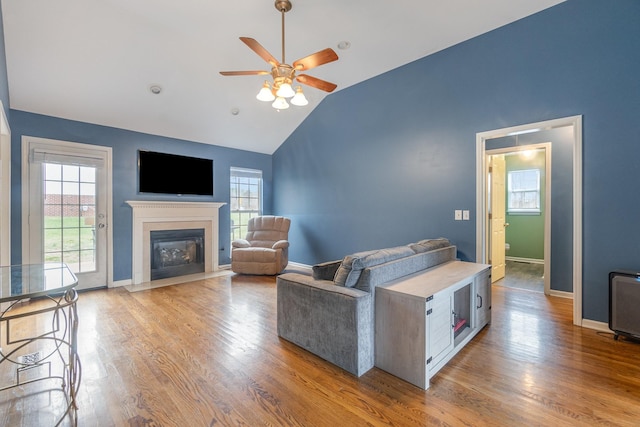 living room featuring a fireplace with flush hearth, a ceiling fan, vaulted ceiling, light wood-type flooring, and baseboards