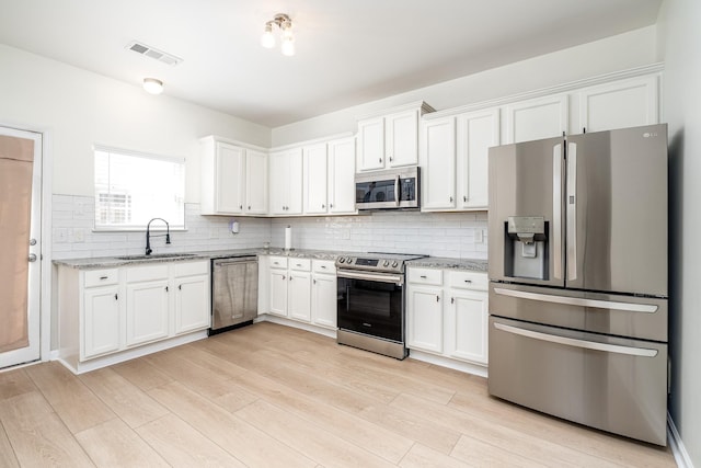 kitchen featuring visible vents, a sink, decorative backsplash, stainless steel appliances, and white cabinetry