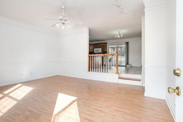 spare room with light wood finished floors, crown molding, and ceiling fan with notable chandelier