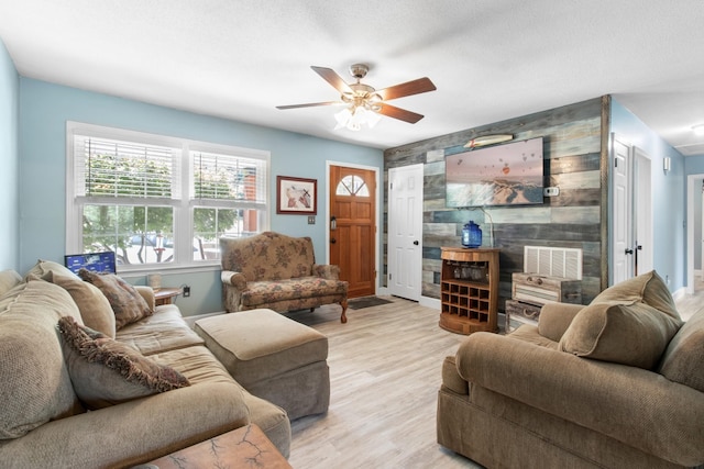 living room with a textured ceiling, ceiling fan, and light hardwood / wood-style flooring