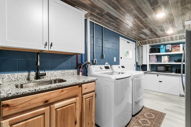 washroom featuring washing machine and clothes dryer, sink, cabinets, light hardwood / wood-style flooring, and wooden ceiling