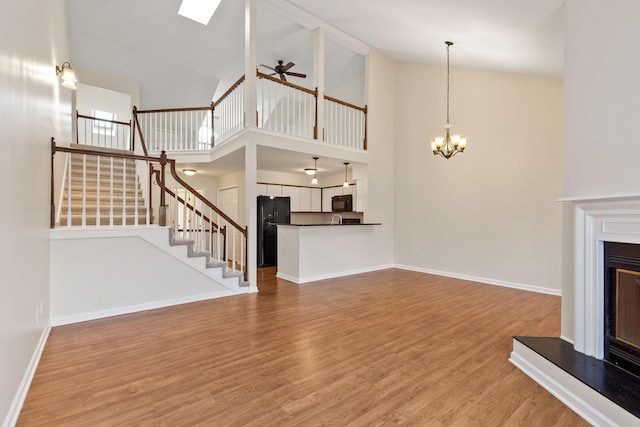 unfurnished living room with hardwood / wood-style flooring, ceiling fan with notable chandelier, and high vaulted ceiling